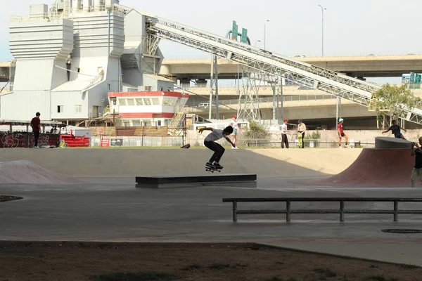 Patinação de menino em um parque de skate em um dia ensolarado com as pessoas e construção em segundo plano — Fotografia de Stock