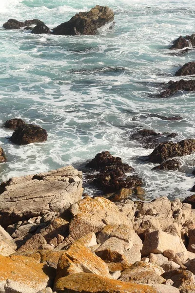 A vertical shot of waves hitting the shore and the rocks in the water