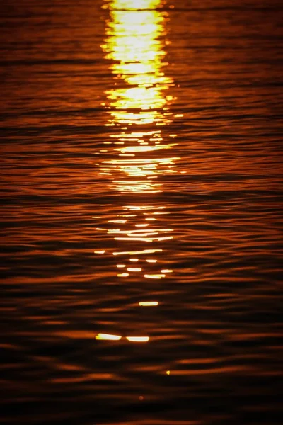 A vertical shot of sea waves reflecting the sunlight at sunset