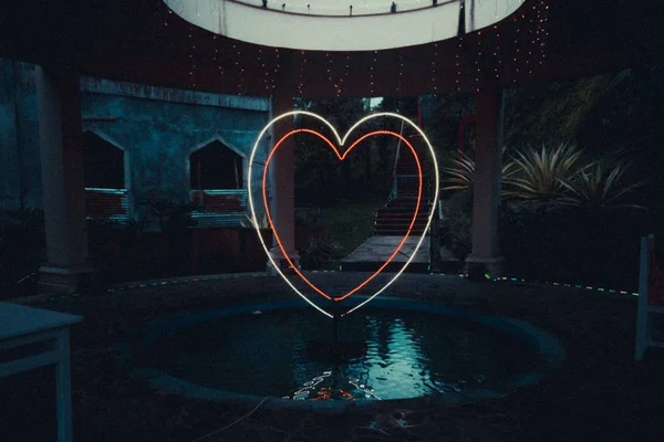 Hermosa piscina en un parque con un corazón de neón con reflejo sobre el agua — Foto de Stock