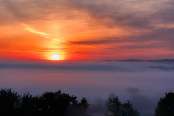 Lindo tiro do pôr do sol incrível com o céu vermelho sobre uma floresta enevoada no campo — Fotografia de Stock