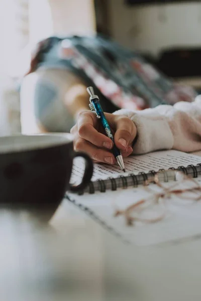 Vertical shot of a female writing something in her notebook with a pen — Stock Photo, Image