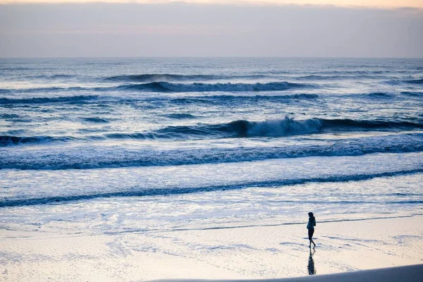 波と曇り空の海の海岸を歩く女性 — ストック写真