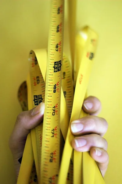 Mão feminina segurando um medidor de medidor amarelo em um fundo amarelo — Fotografia de Stock