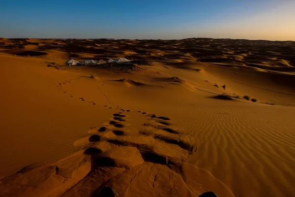 Vackert skott av fotspår i sanddyn med vita tält i fjärran och en klar himmel — Stockfoto