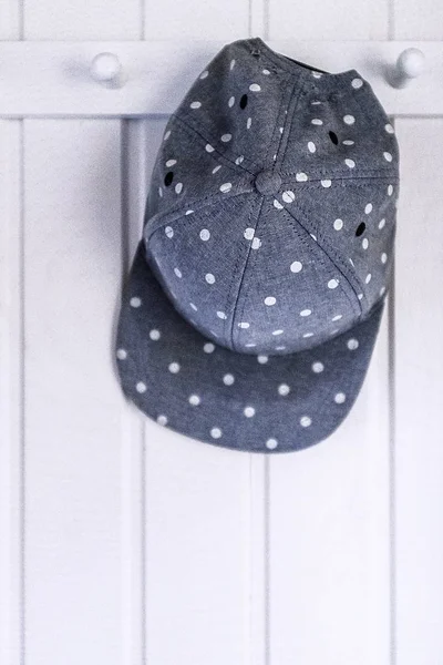 Tečkovaný klobouk zavěšený na bílém dřevěném šatníku — Stock fotografie