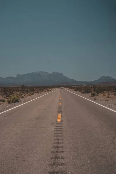 Tiro vertical de una carretera que atraviesa el desierto con montañas al fondo — Foto de Stock