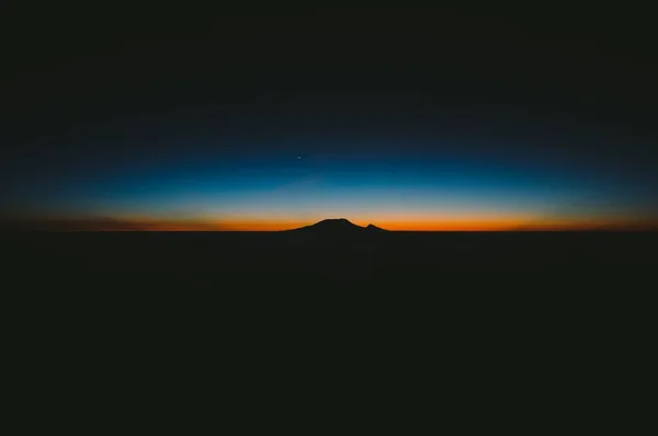 Hermosa toma de colinas oscuras con la increíble puesta de sol naranja y azul en el horizonte —  Fotos de Stock