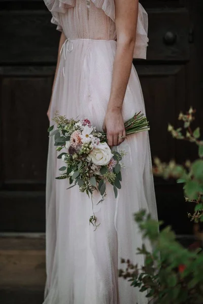 Tiro vertical de uma noiva usando vestido de noiva segurando um buquê de flores — Fotografia de Stock