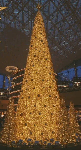 Gyönyörű arany sárga fényes karácsonyfa egy modern épületben — Stock Fotó