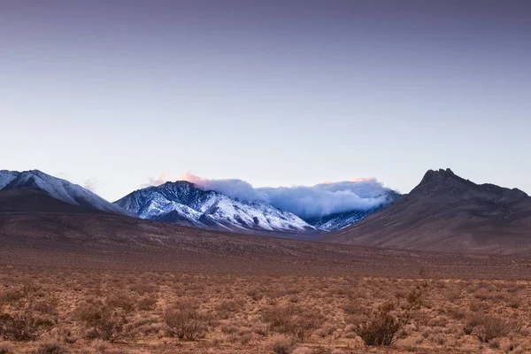 Colcha nublada sobre las montañas nevadas rodeadas de desierto —  Fotos de Stock