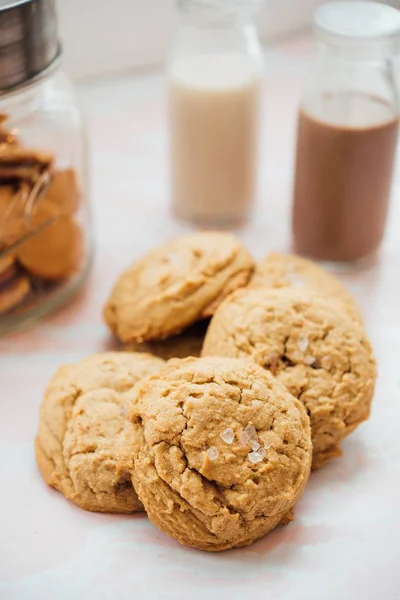 Fotografie verticală de închidere a cookie-urilor gustoase pe o suprafață albă cu lapte de ciocolată în fundal — Fotografie, imagine de stoc