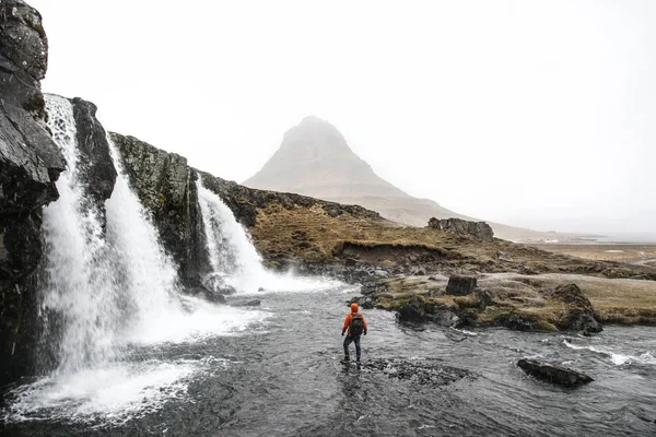Belle prise de vue d'une personne debout dans l'eau près des cascades coulant sur les collines — Photo