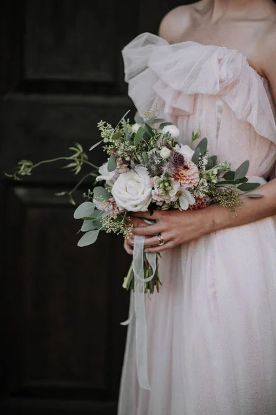 Tiro vertical de uma noiva usando vestido de noiva segurando um buquê de flores — Fotografia de Stock