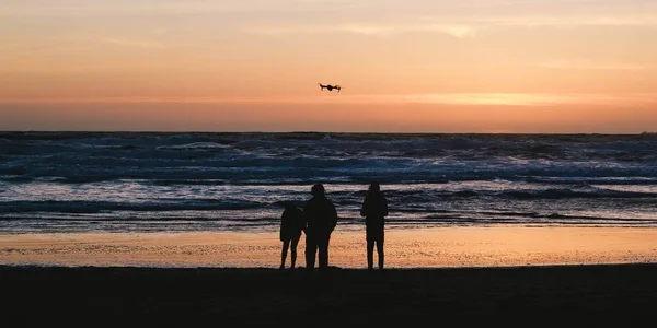 Silhuetas de pessoas em pé na praia e desfrutando do belo pôr do sol — Fotografia de Stock