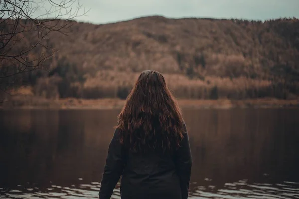 Kobieta z długimi włosami patrząca na piękne jezioro w lesie — Zdjęcie stockowe