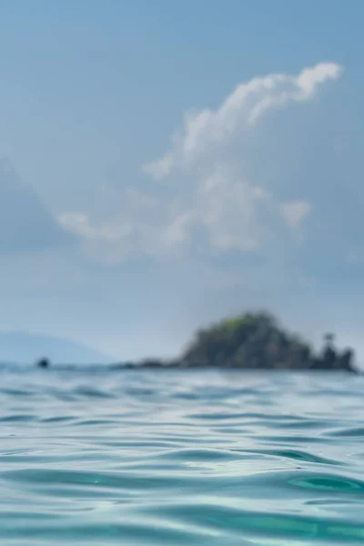 Closeup shot of the ocean water taken slightly above the water with small island in the background — Stock Photo, Image