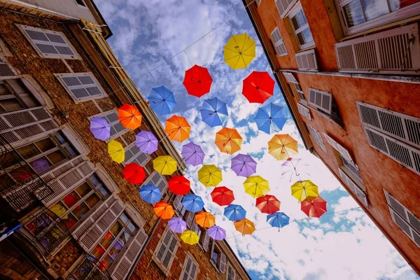 Colpo basso di ombrelli colorati appesi nel mezzo di edifici con cielo nuvoloso — Foto Stock