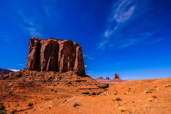 Collina rocciosa con una grande roccia desertica vicino a cespugli secchi e un cielo blu sullo sfondo — Foto Stock