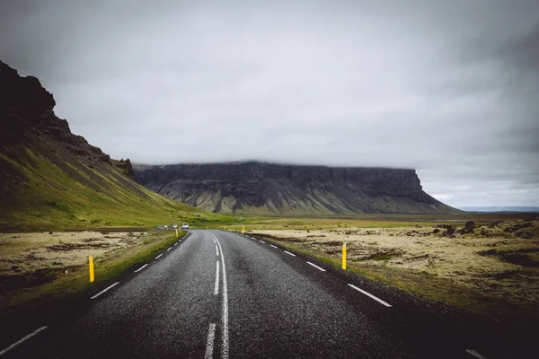 Une route mince dans un champ verdoyant avec des collines et un ciel gris nuageux en Islande — Photo