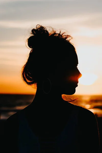 Silhouet van een vrouwtje dat aan de kust van de zee staat met een prachtige zonsondergang op de achtergrond — Stockfoto