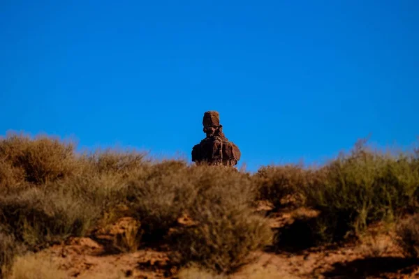 Selektive Fokusaufnahme einer Wüstenklippe über einem Hügel mit getrockneten Büschen und klarem Himmel im Hintergrund — Stockfoto
