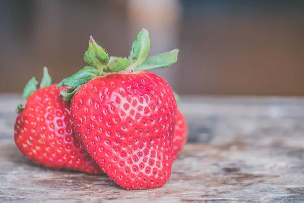 Nahaufnahme frischer reifer Erdbeeren auf einem unscharfen hölzernen Hintergrund — Stockfoto