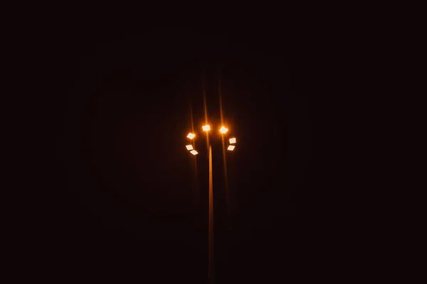 Világító lámpaoszlop távolsági fényképe koromfekete területen — Stock Fotó