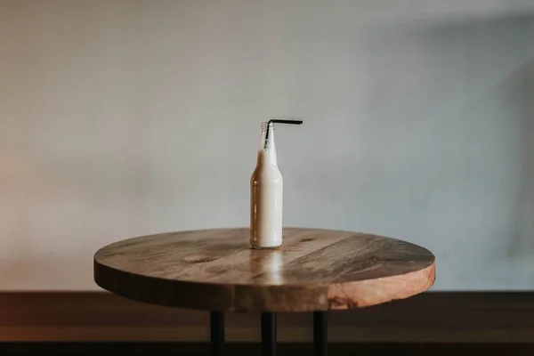 Tournage d'une bouteille en verre avec une paille noire remplie d'une boisson sur une table en bois marron — Photo