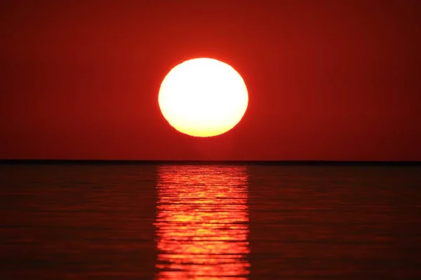 Long range shot of  sea reflecting the sun with the red sky in the background at sunset — Stock Photo, Image