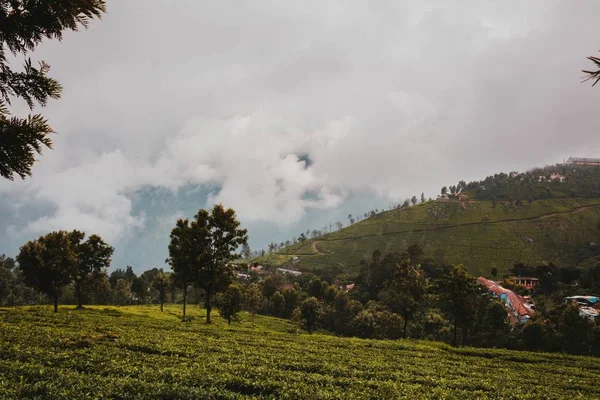 Um belo campo verde perto de uma pequena cidade e céus nublados sobre as colinas — Fotografia de Stock