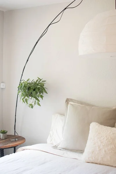 Tiro vertical de uma cama branca com travesseiros e uma cama de madeira redonda ao lado dela com uma planta pendurada — Fotografia de Stock