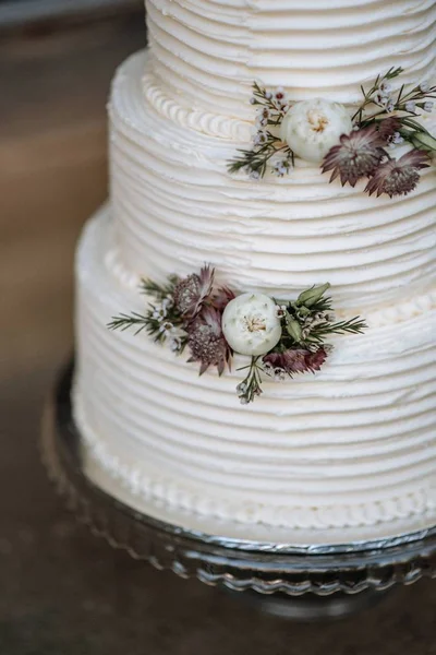 Primer plano vertical de un pastel de boda de tres capas decorado con flores en una bandeja de plata — Foto de Stock