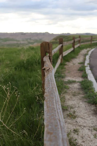 Vertikální záběr dřevěného plotu uprostřed silnice a travního pole — Stock fotografie