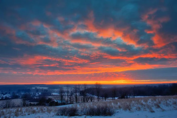 Beautiful shot of amazing red and orange clouds over large misty fields and forest at dawn — Stock Photo, Image