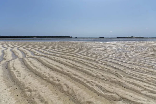 Praia de areia com ondas padrão ondulações linhas com água em um dia ensolarado — Fotografia de Stock