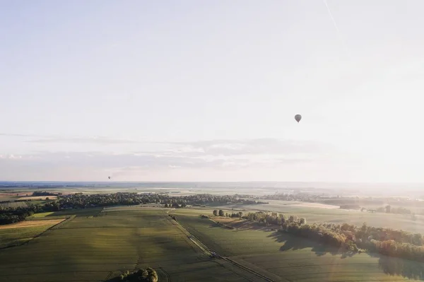 Amplo tiro de prados verdes cercados por árvores sob um céu limpo com um balão de ar alto flutuando — Fotografia de Stock
