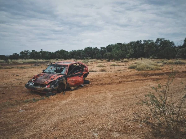 Viejo coche roto en un campo de hierba seca con árboles en el fondo — Foto de Stock