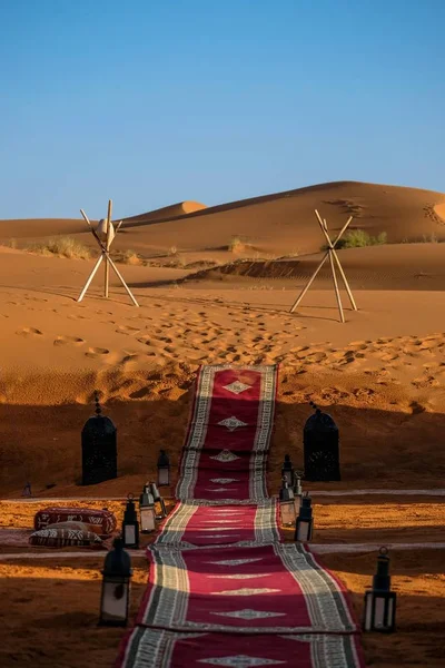 Vertical shot of a red carpet in the middle of lamps and stick tripod with a rock in the distance — Stock Photo, Image