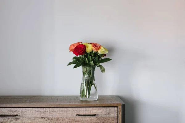 Belo buquê de rosas coloridas em um frasco de vidro em um armário de madeira — Fotografia de Stock