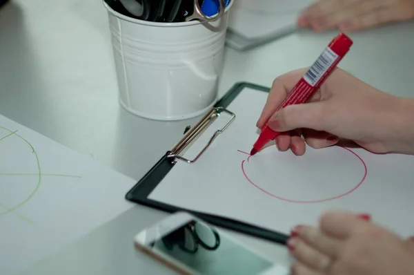 Closeup shot of a female drawing a circle with a red marker on white paper — Stock Photo, Image