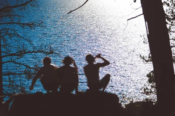 Силует друзів, що сидять на скелі біля мальовничого озера Тахо (Каліфорнія), відбиває сонячне світло. — стокове фото