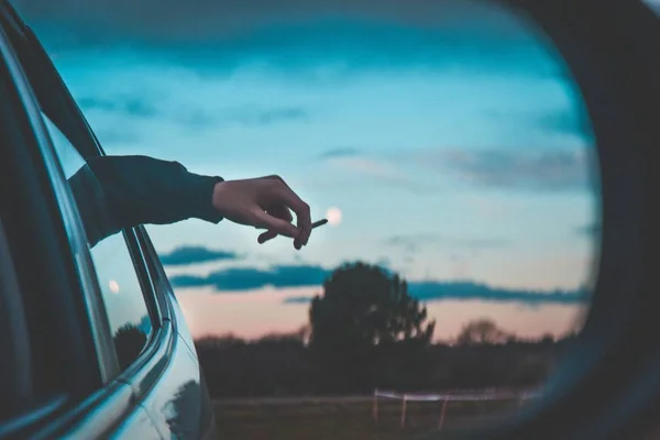 Mano de la persona sosteniendo un cigarrillo y saliendo por la ventana del asiento trasero de un coche — Foto de Stock