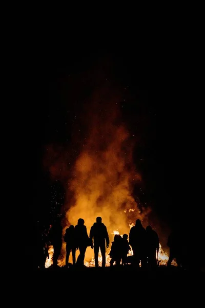 Silhouettes of people gathered around a large bonfire in the woods