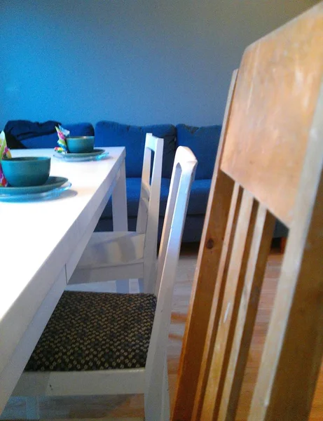 Colpo verticale di tazze di ceramica blu su un tavolo bianco con sedie sul lato vicino a un divano blu — Foto Stock