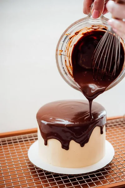 Fechar-se de um delicioso bolo com o padeiro derramando creme de chocolate sobre ele — Fotografia de Stock