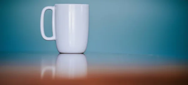 Weiße Tasse auf reflektierender Oberfläche mit blauem Hintergrund und Platz für Text — Stockfoto