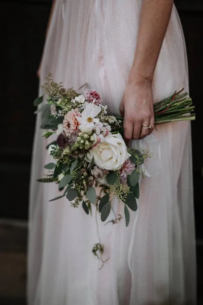 Tiro vertical de uma noiva usando vestido de noiva segurando um buquê de flores — Fotografia de Stock