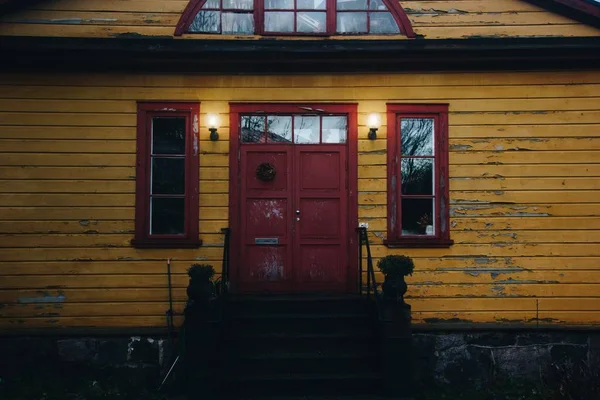 Entrada de uma grande casa de madeira com uma porta vermelha enferrujada e janelas em ambos os lados — Fotografia de Stock
