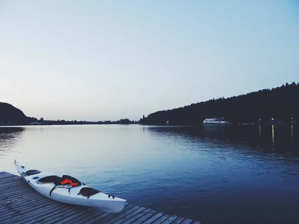 Beautiful shot of a lake with a white kayak on a brown wooden dock — Stock Photo, Image